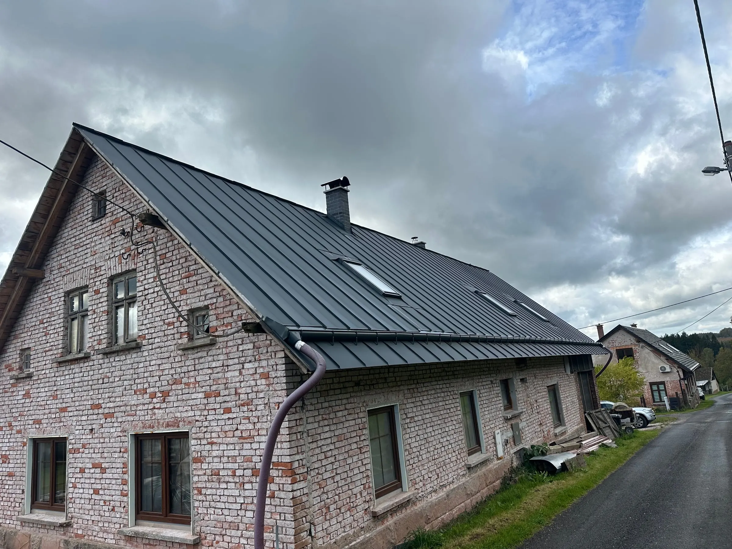 Starý cihlový dům s novou tmavou falcovanou plechovou střechou a střešními okny