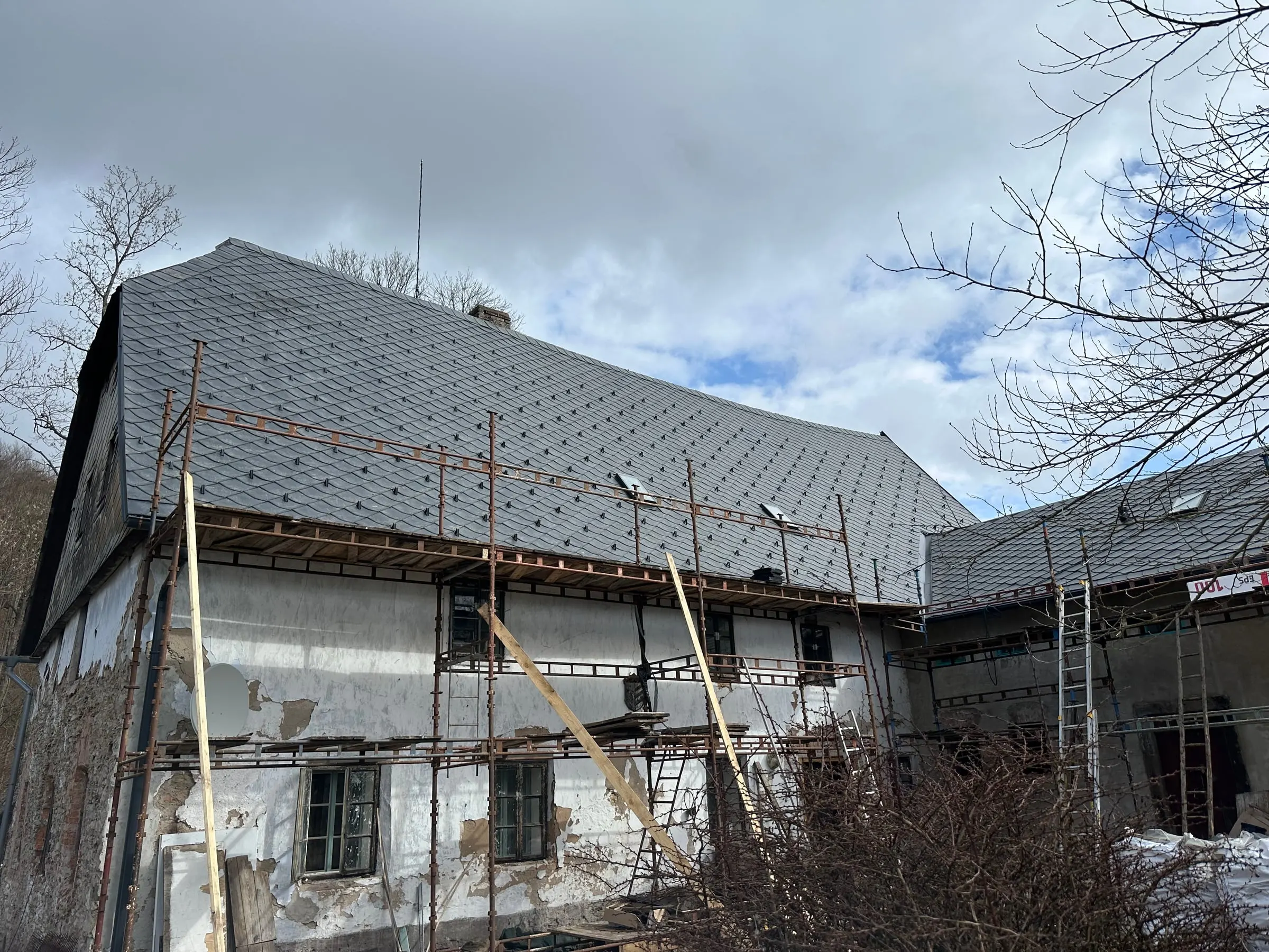 Velké staré stavení s novou maloformátovou krytinou, u opadané fasády stojí lešení