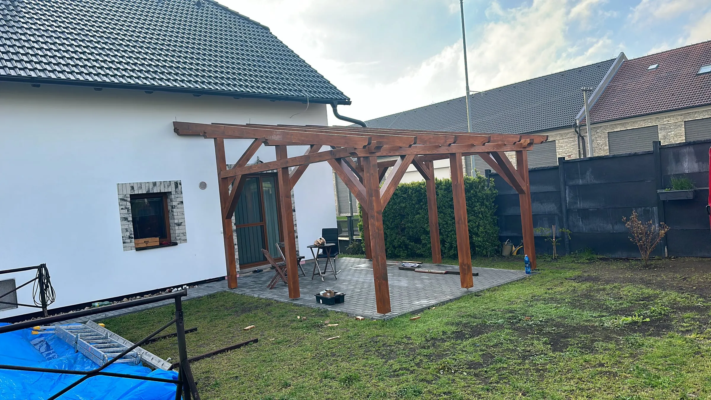 Dřevěná pergola s šikmými vzpěrami na zahradě u bílého domu
